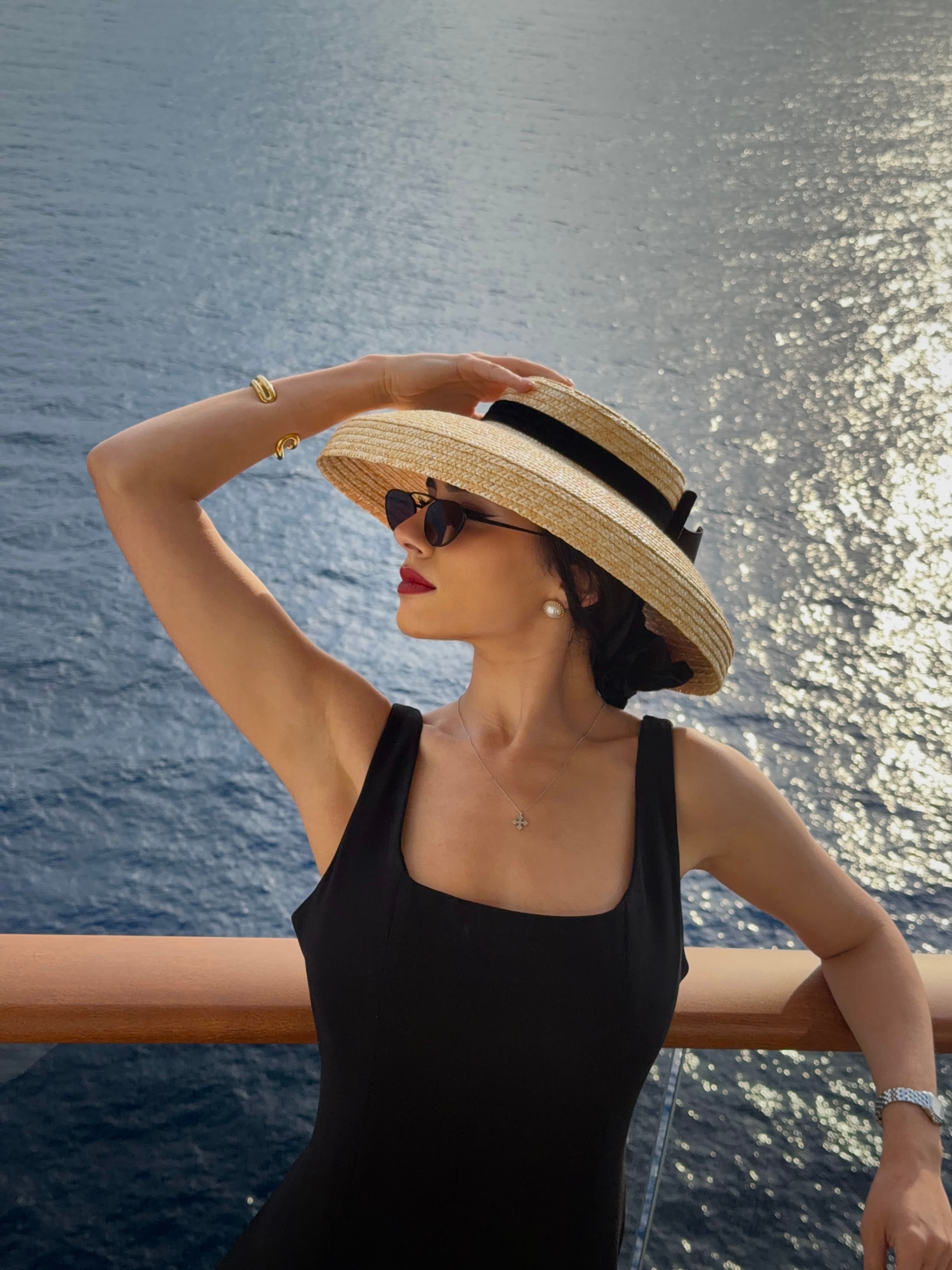 Chryssa Handis wearing a classic black dress and straw hat by the sea